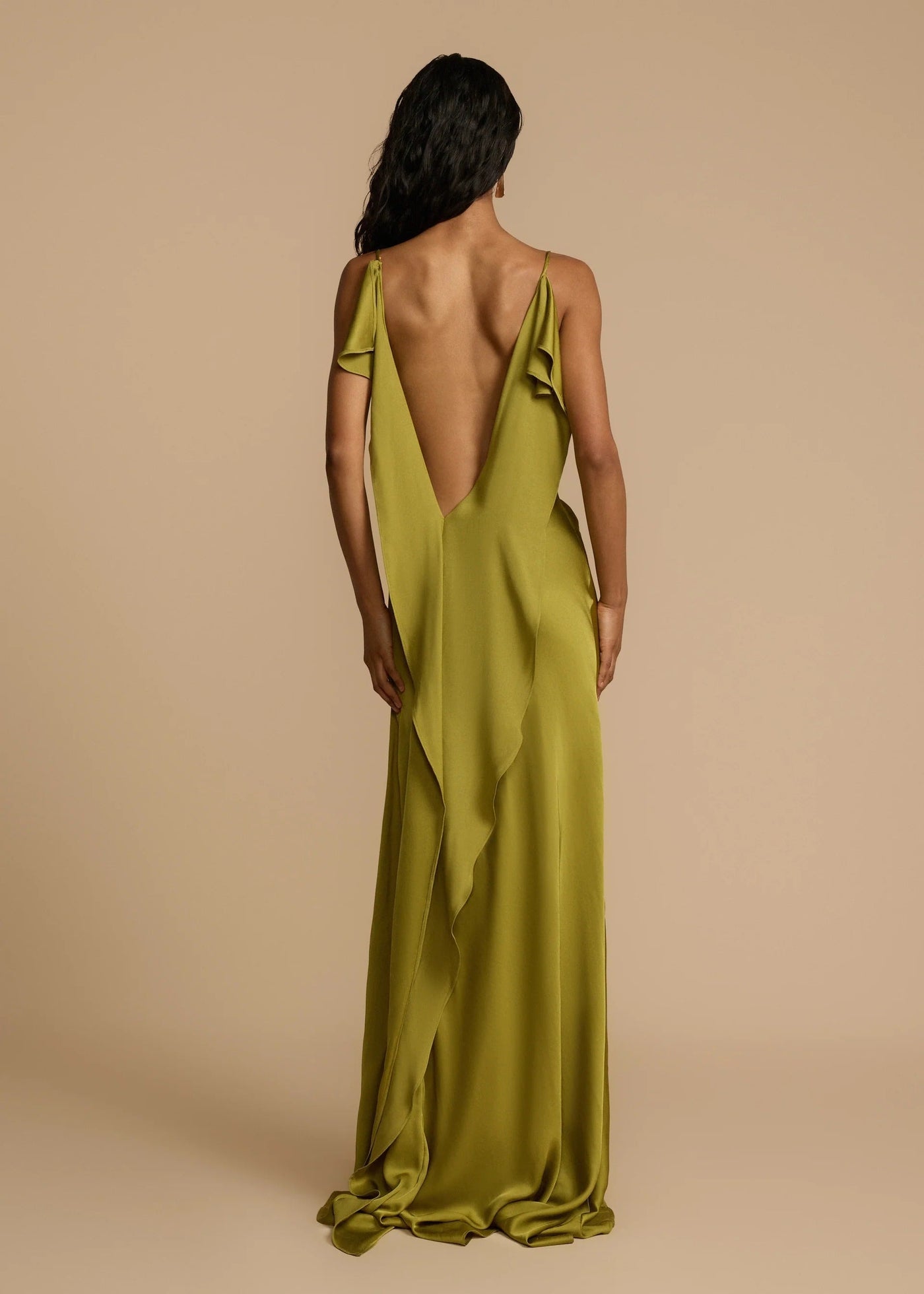 Woman wearing a green evening gown with a deep back on a beige background