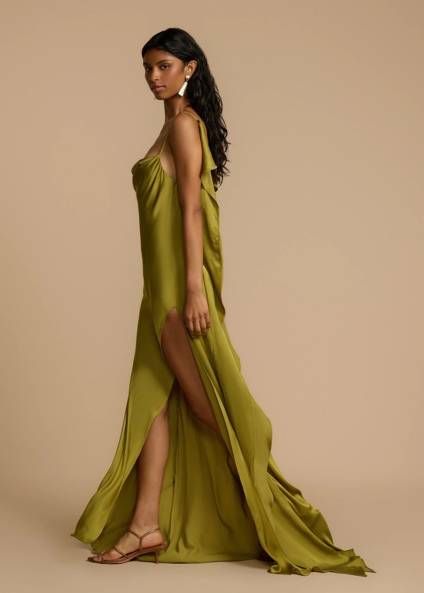 Woman wearing a green dress with a slit on a beige background