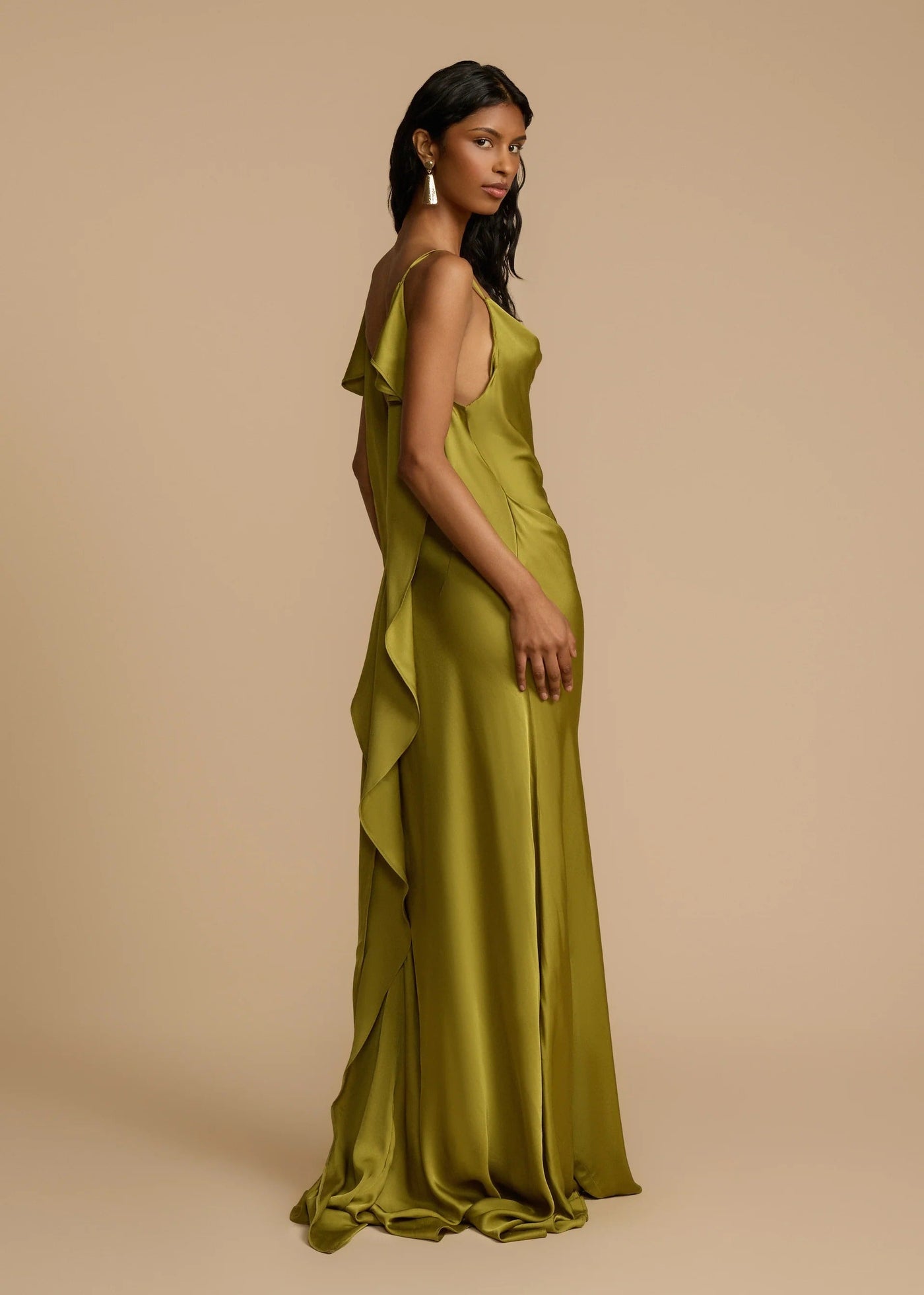 Woman wearing a green gown with ruffled details on a beige background