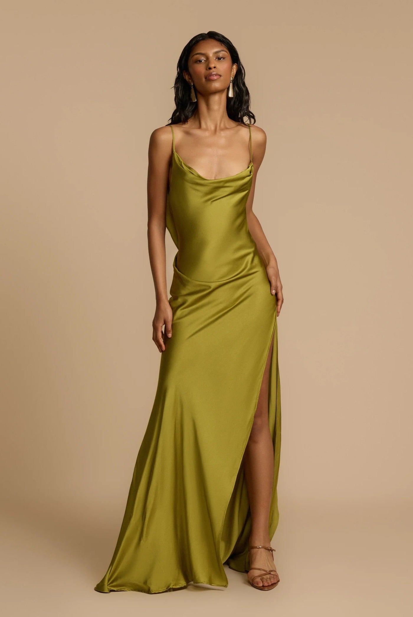 Woman wearing a green satin dress with a slit on a beige background