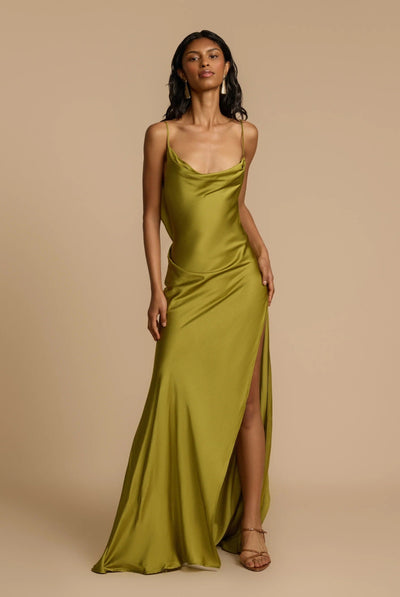Woman wearing a green satin dress with a slit on a beige background